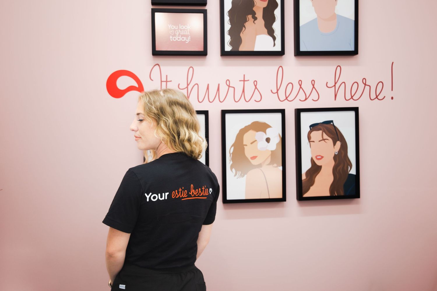 Person in black shirt views portrait gallery wall with pink neon sign.