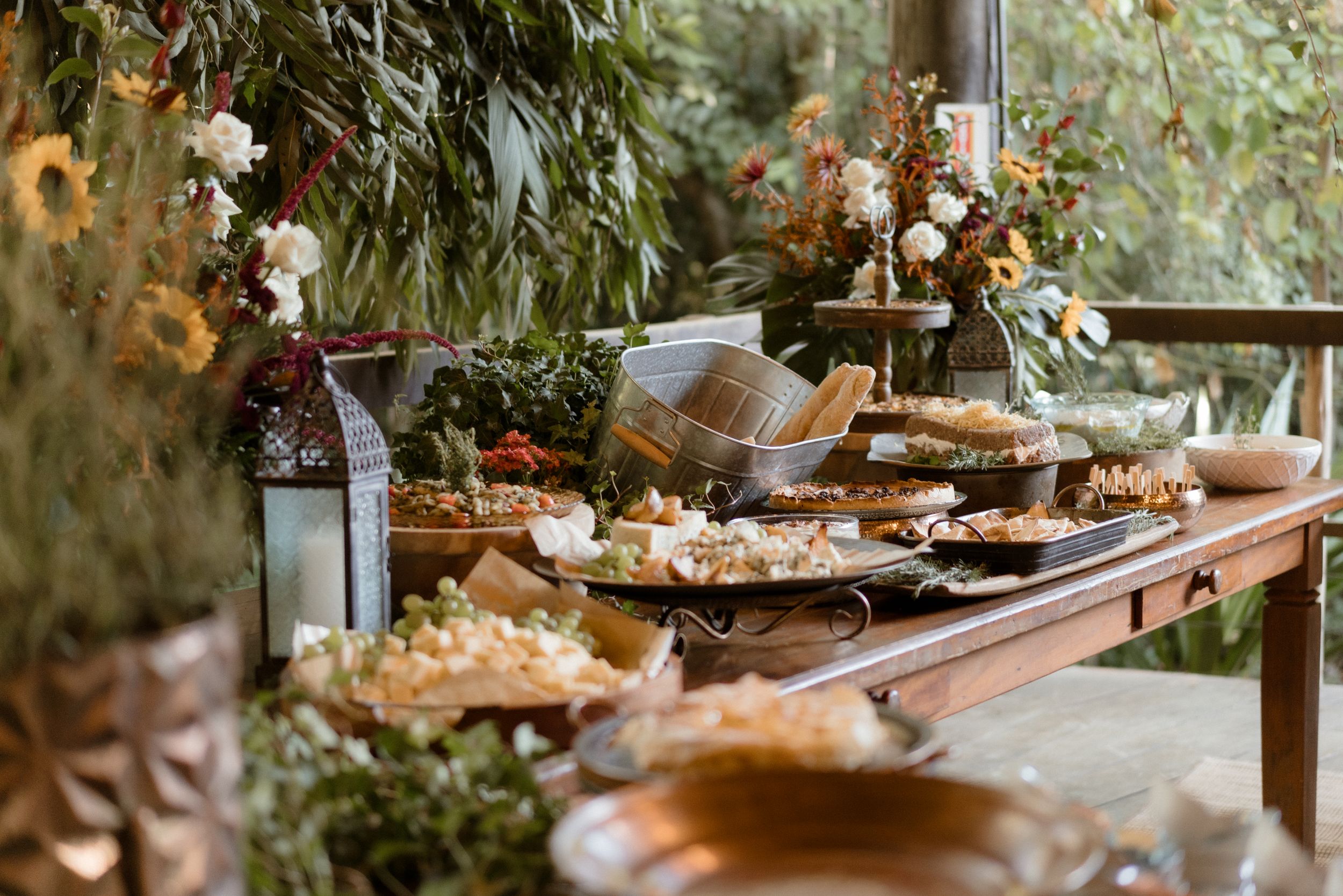 Catering display of appetizers and snacks arranged on wooden tables with natural greenery.