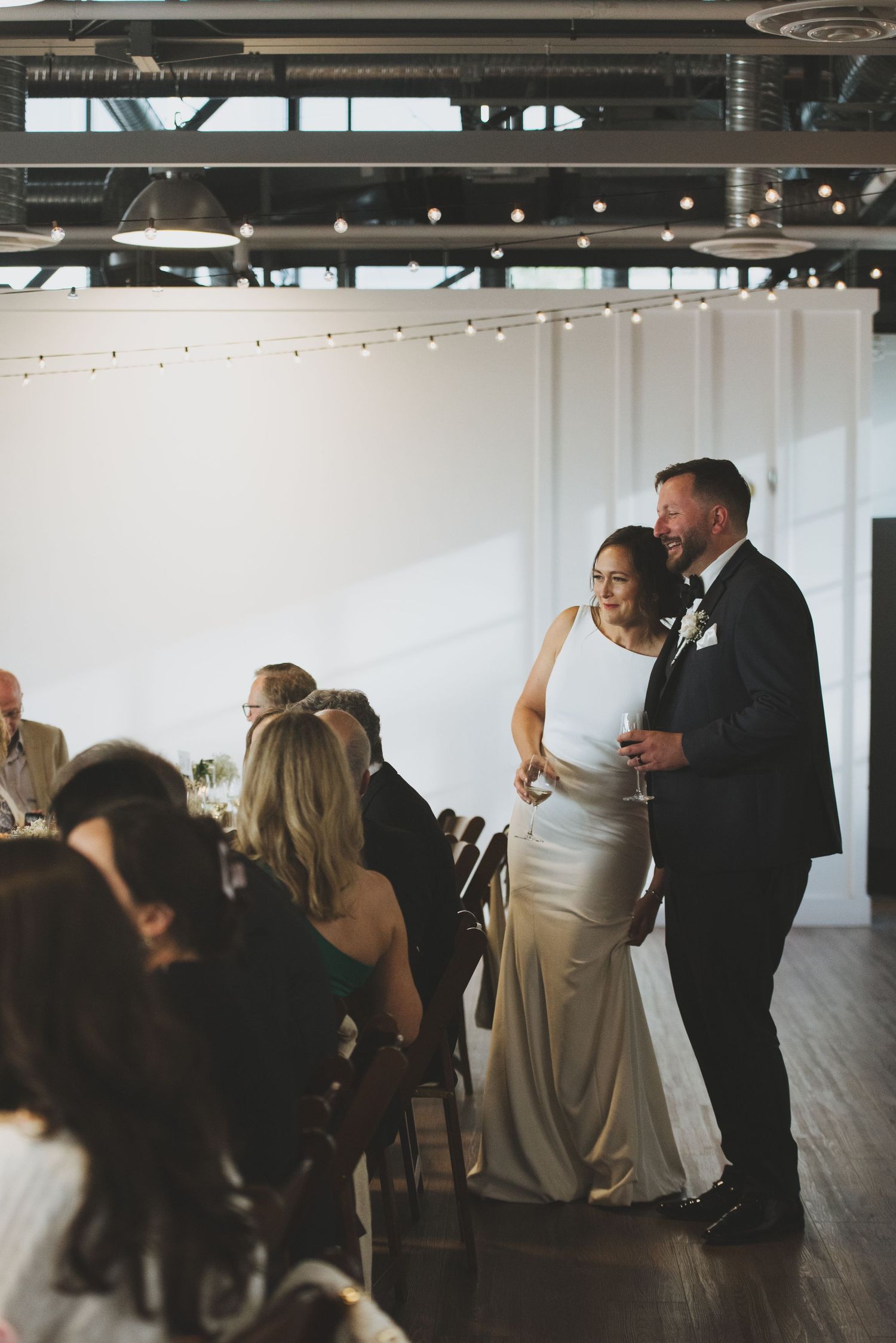 Wedding reception in a modern venue with string lights and industrial ceiling.