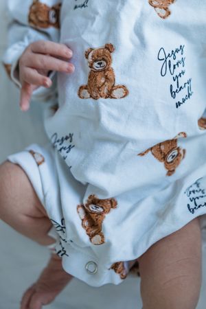 Close-up view of white baby clothing with cute brown teddy bear pattern print details.