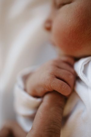 Close-up shot of tiny baby hand grasping white fabric.