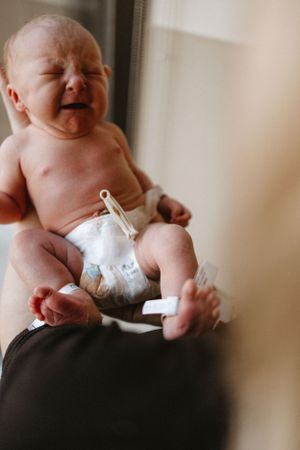 Crying newborn baby wearing diaper during medical examination.
