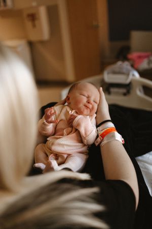 Sleeping newborn in pink outfit resting on caregiver's lap.