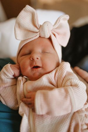 Newborn baby wearing pink knit outfit with matching bow hat sleeping peacefully.