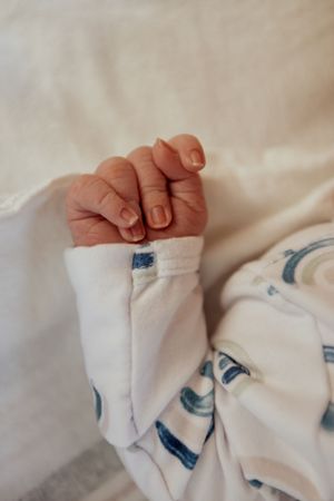 Close-up of a tiny baby hand with delicate fingernails against white fabric with blue pattern details.