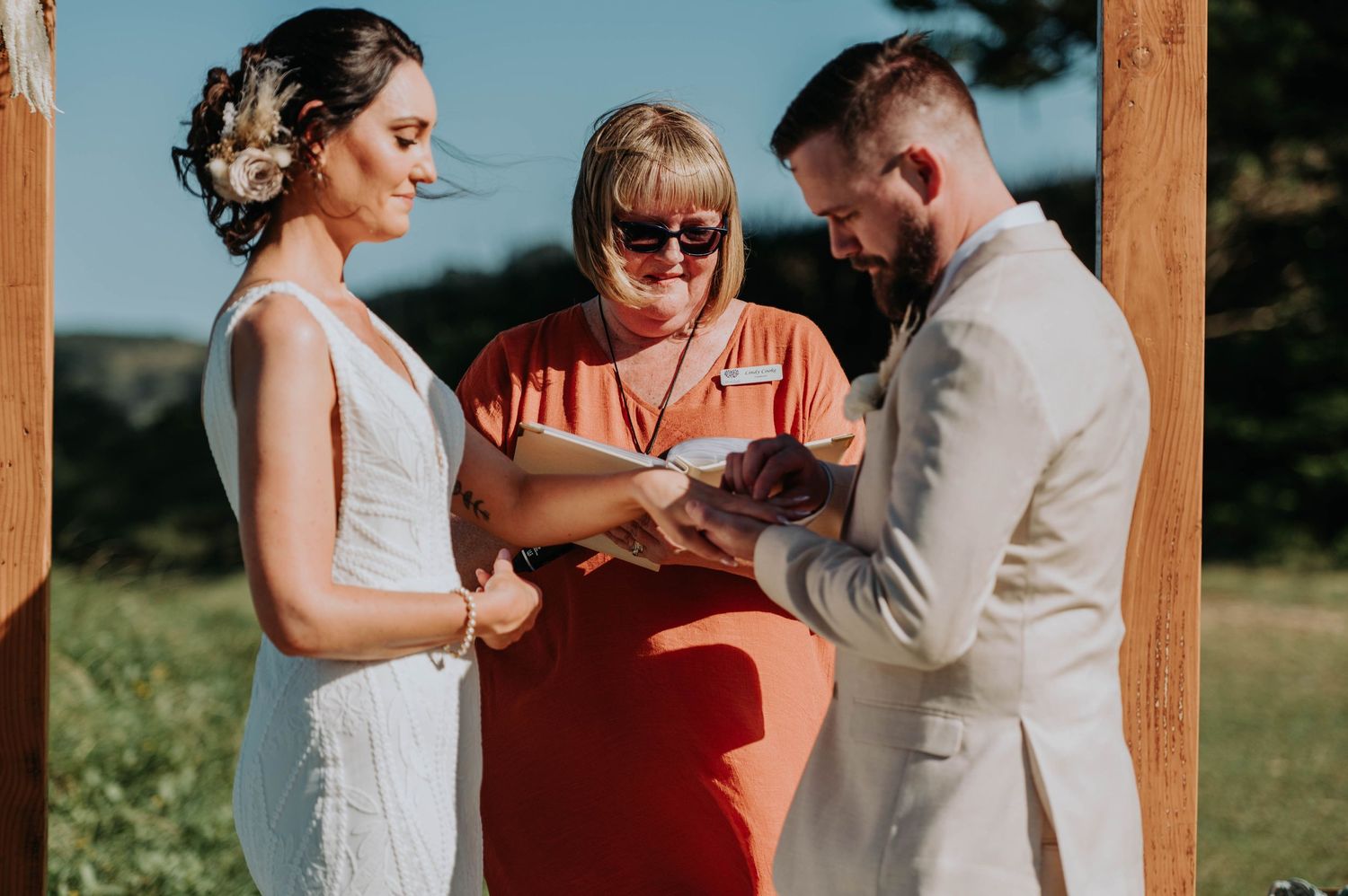 Wedding ceremony under wooden arch with participants reviewing documents.