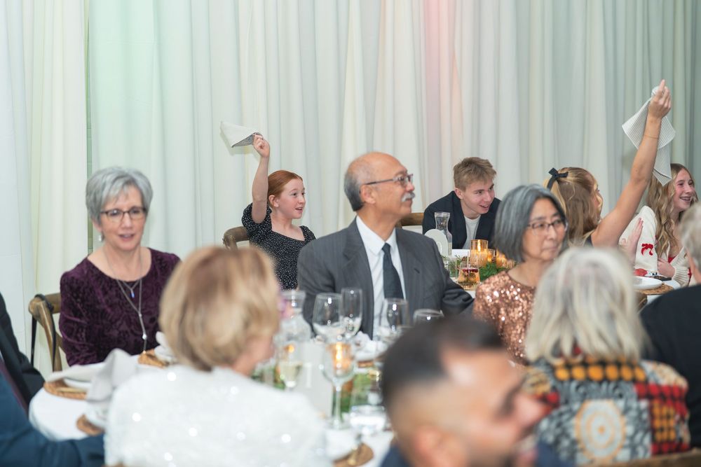 Large group of people gathered at tables for a formal dining event in a bright banquet hall.
