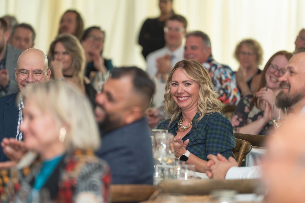 Crowd of attendees socializing and laughing during a holiday celebration in a decorated venue.