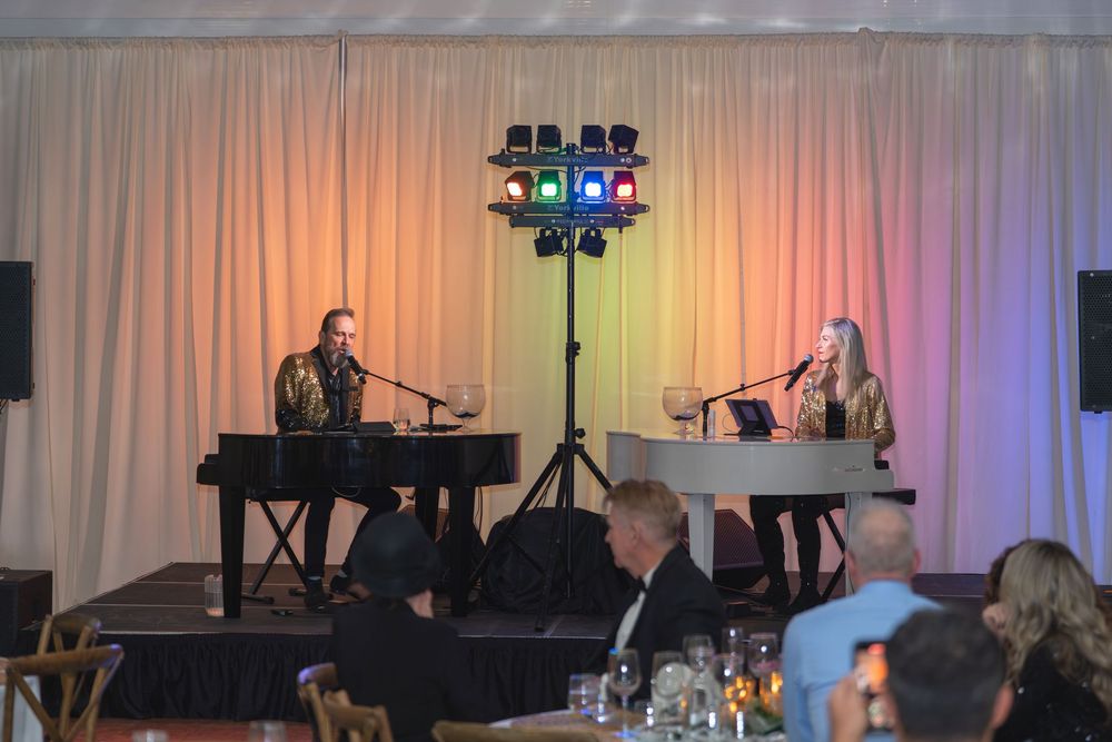 A live band performs on stage with colorful lighting and white curtain backdrop during an indoor event.