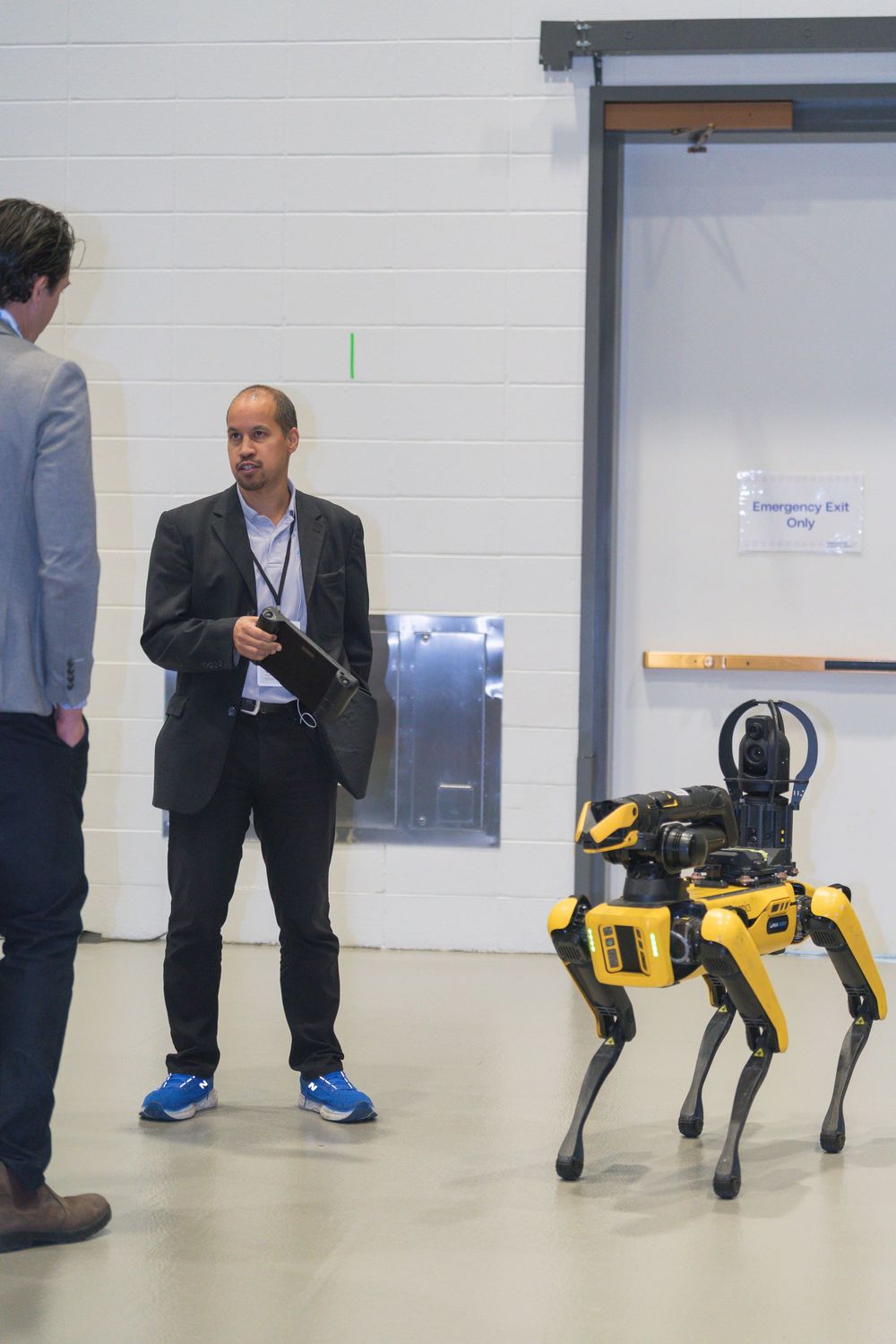 A yellow robotic dog walks alongside people in business attire in an office hallway.