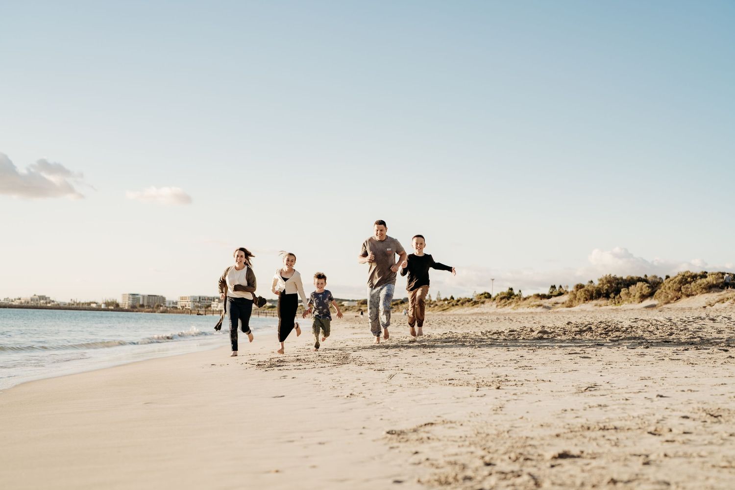 Family running and playing together on a sunny beach with clear blue skies.