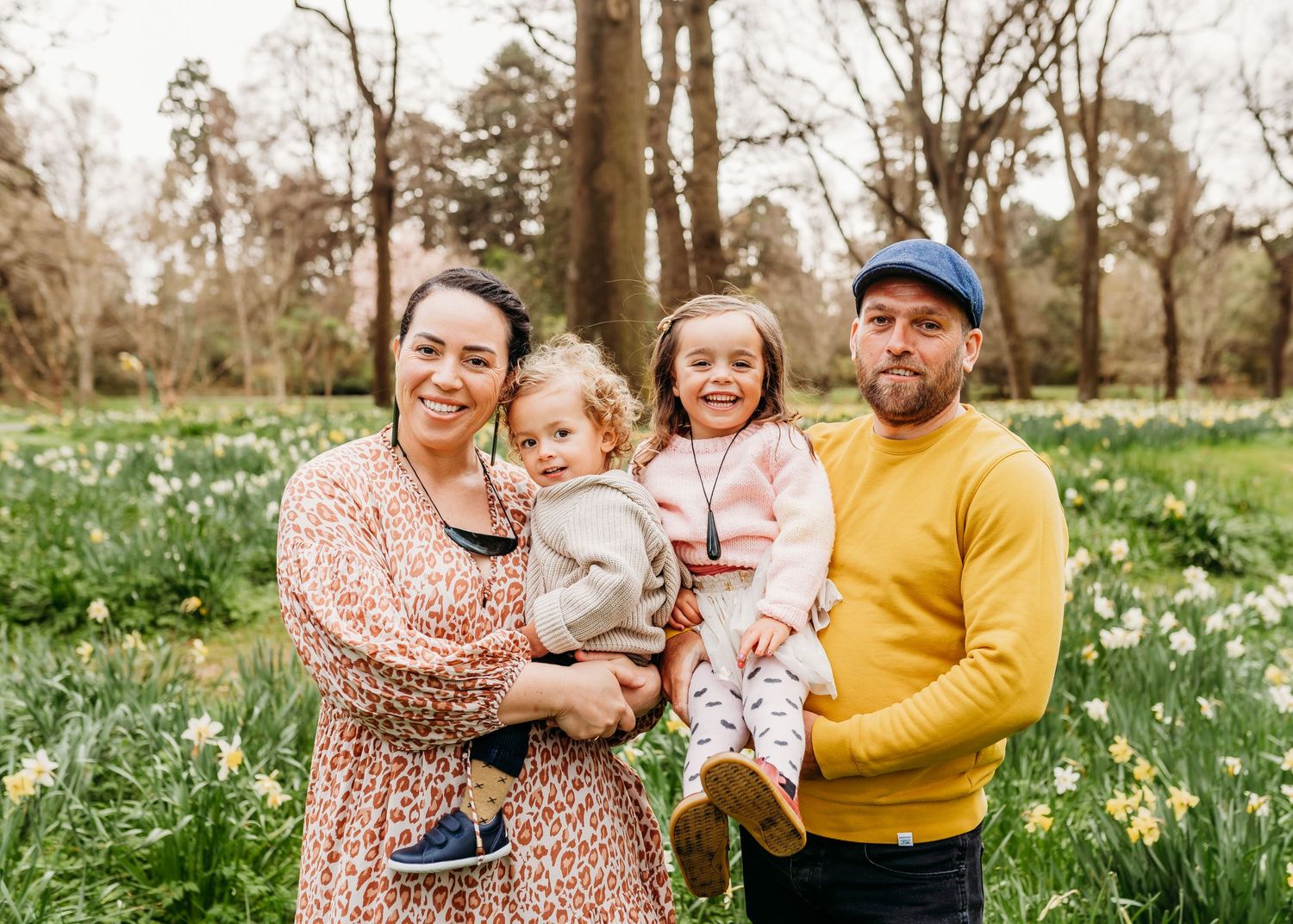 Family of four posing together in a spring meadow filled with daffodils.
