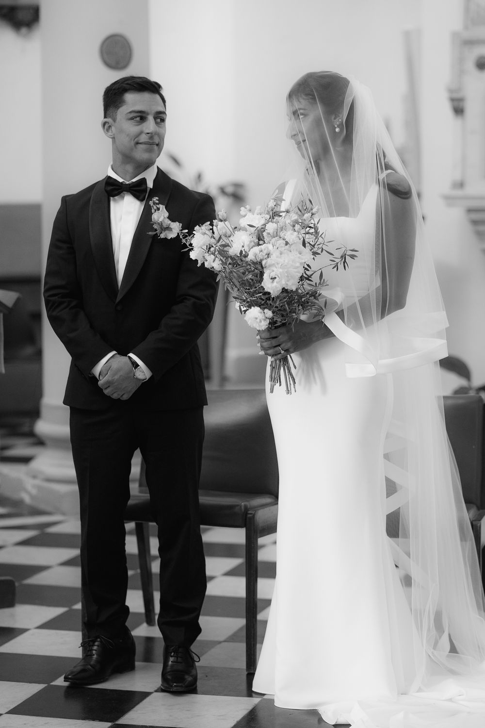 Wedding ceremony in progress on black and white checkered floor of a church.