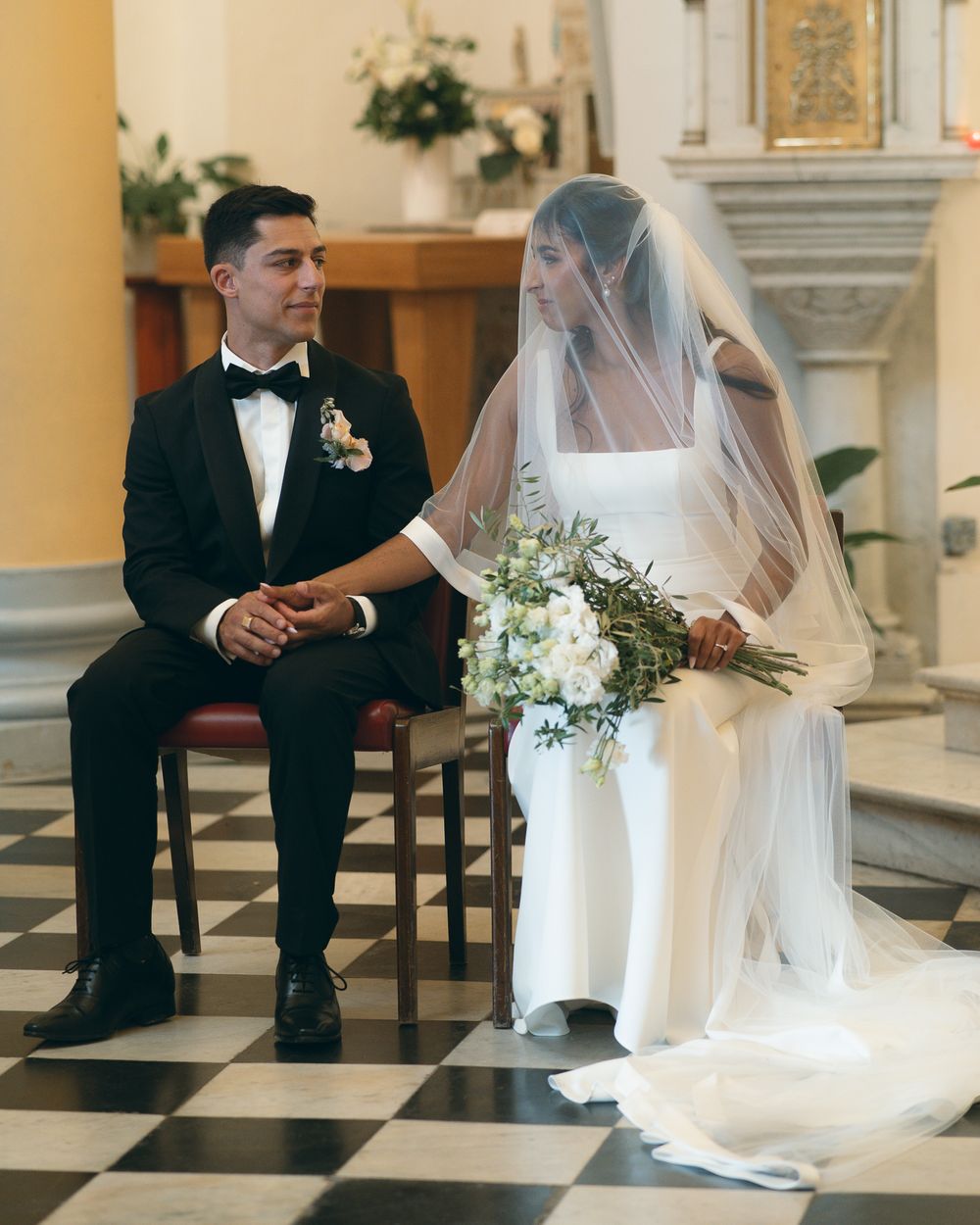 Wedding ceremony in a church with yellow walls and checkerboard flooring.