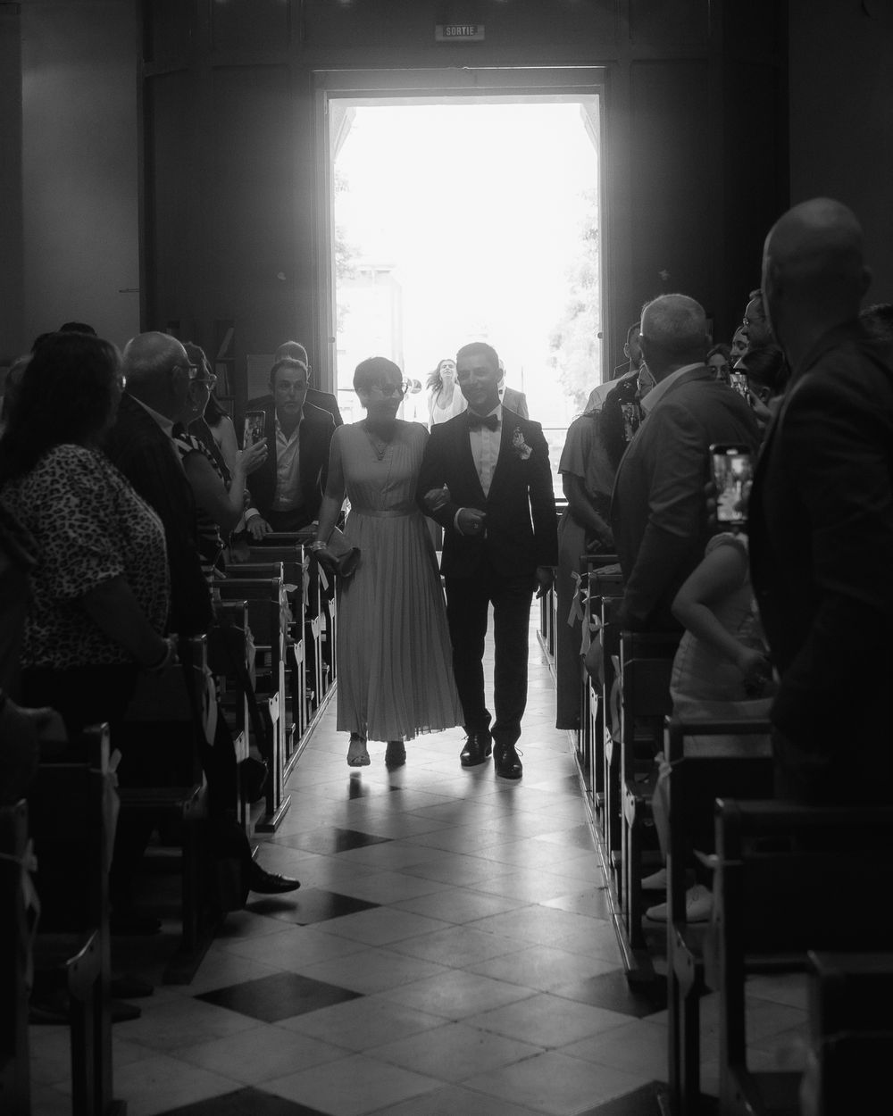 Silhouetted figures in church pews with bright window light streaming in.