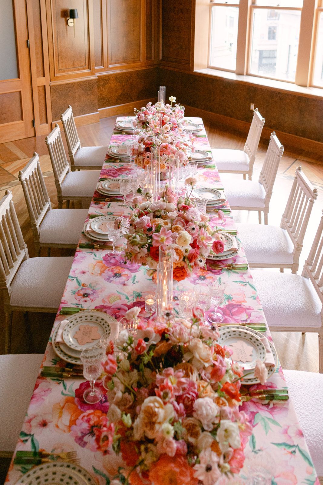 Elegant table setting with crystal glasses, floral tablecloth, and pink flower centerpiece for romantic dining experience.