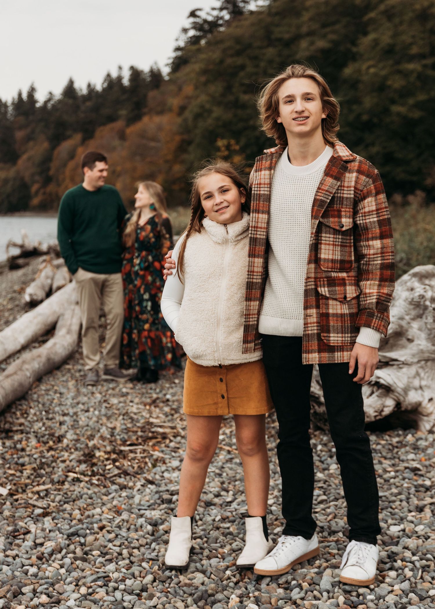 Group in fall casual wear standing on rocky beach with autumn trees in background.