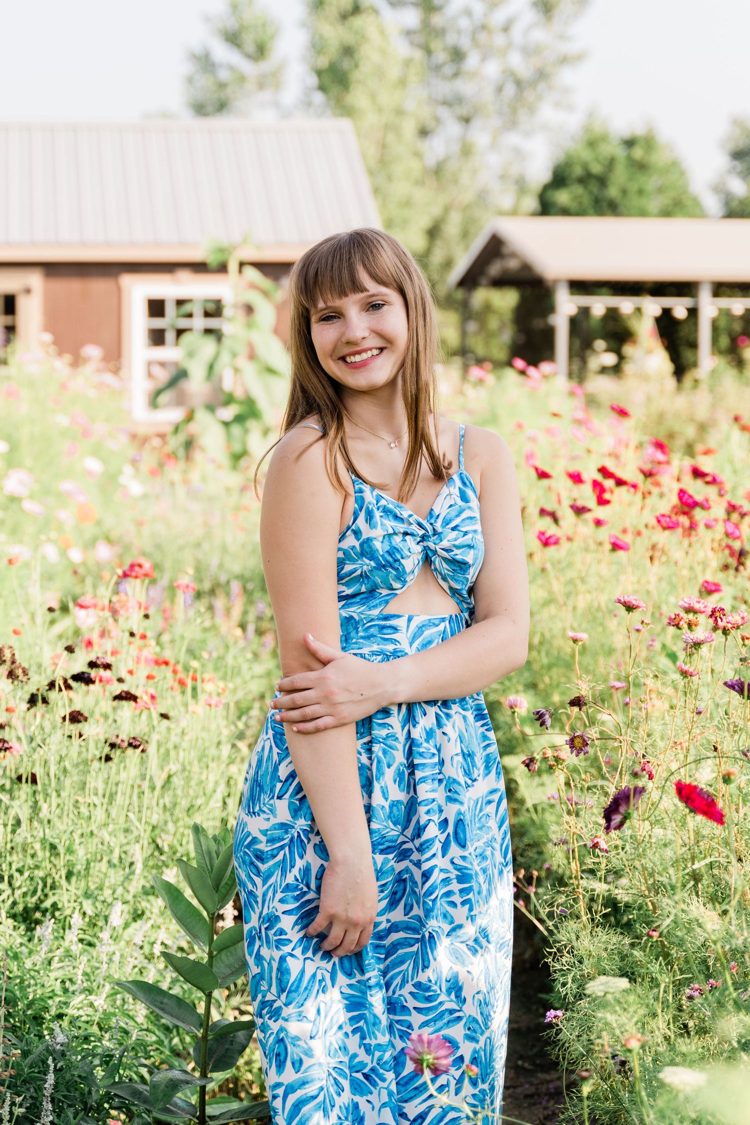 Anthony Wayne High School senior in a blue and white floral dress stands smiling in a garden of red poppies for her summer photo session.