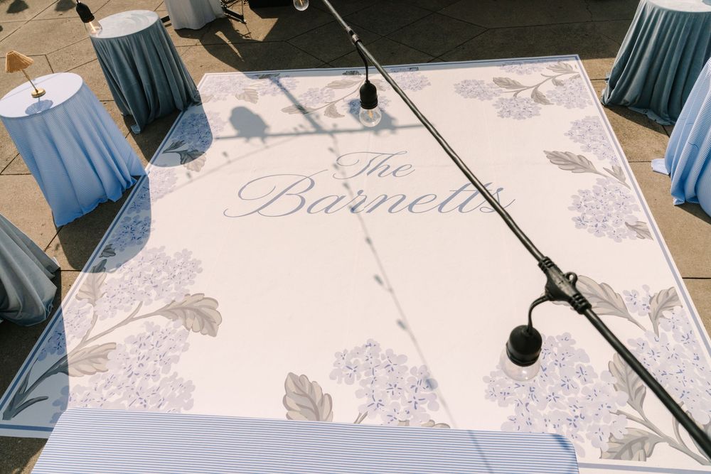 Custom white wedding dance floor with blue hydrangea floral design and elegant script reading The Barnetts.