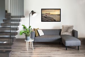 Modern living room interior with grey sectional sofa, floating staircase, framed coastal artwork and potted plant.