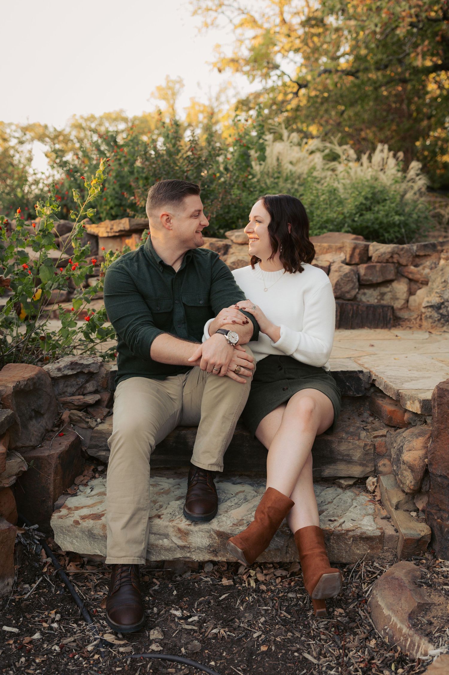 A couple sits together on rustic stone steps surrounded by autumn foliage during a romantic outdoor photoshoot.