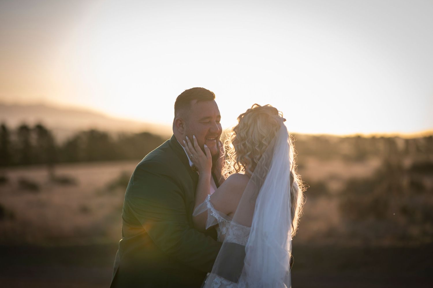 Silhouette of a couple in wedding attire embracing during golden sunset with mountains in background.