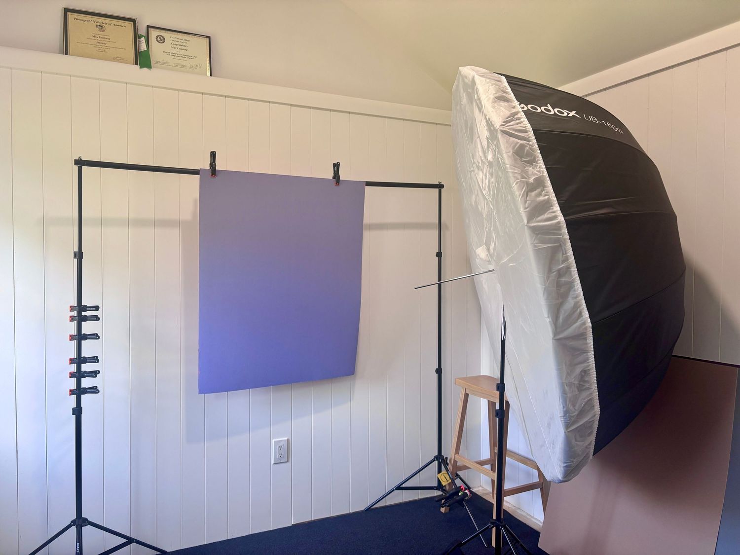 Photography studio setup with purple backdrop on stand and large Godox umbrella softbox lighting equipment.