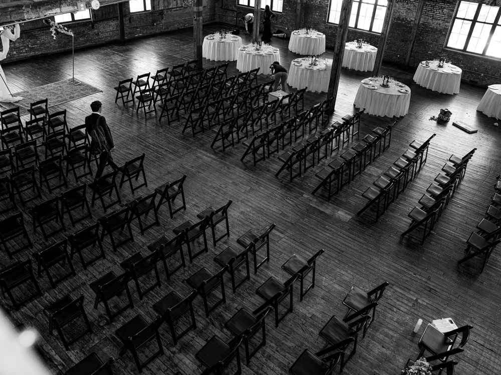 Empty wedding ceremony space with rows of chairs and round reception tables in an industrial venue.