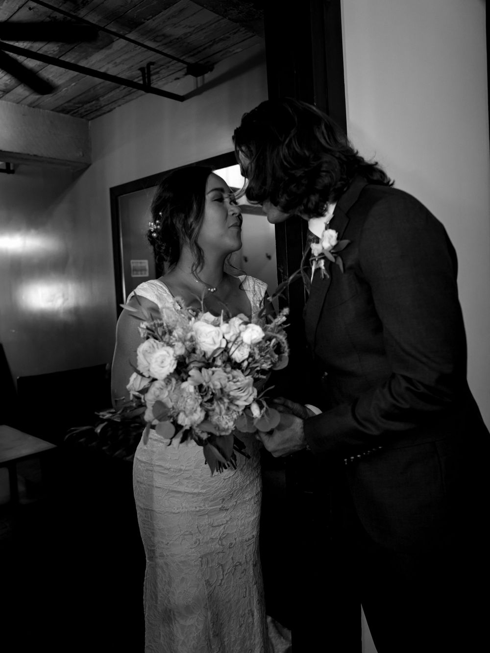 Black and white portrait of wedding couple with elegant bouquet in minimalist indoor setting.