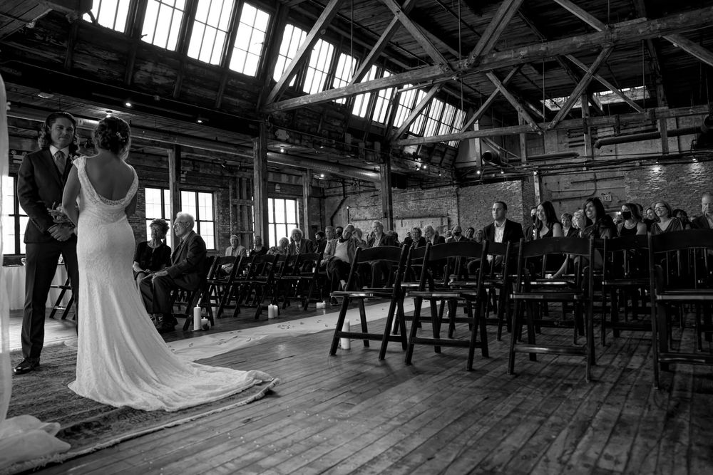 Black and white wedding ceremony setup in industrial venue with high windows and wooden floors.