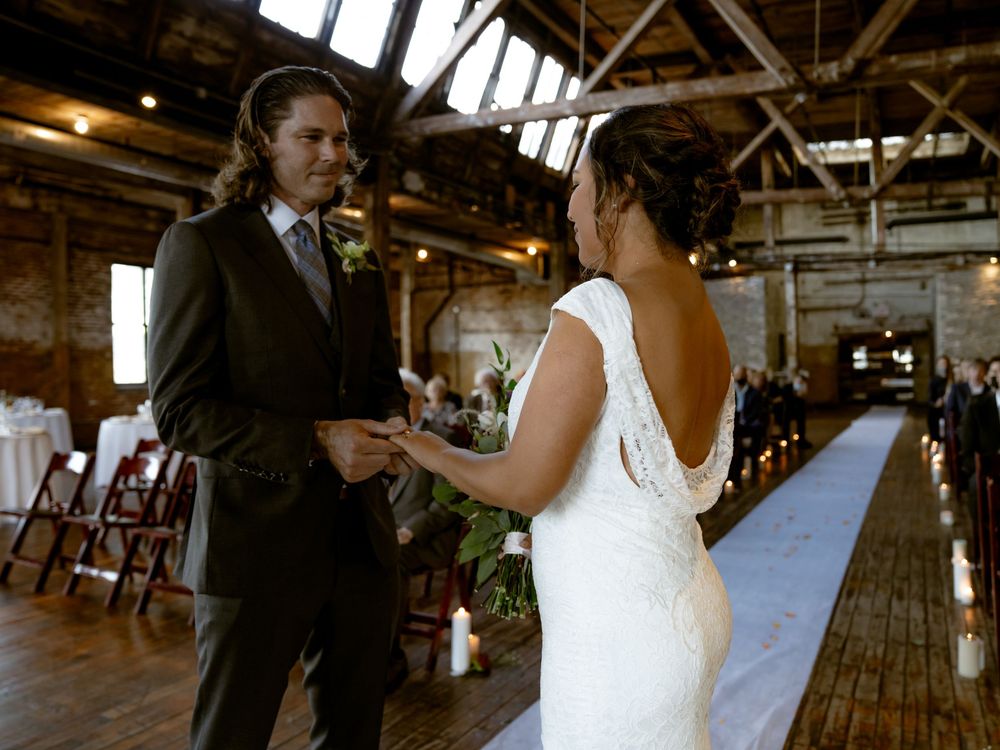 Intimate wedding ceremony moment in rustic industrial venue with wooden beams and natural light.