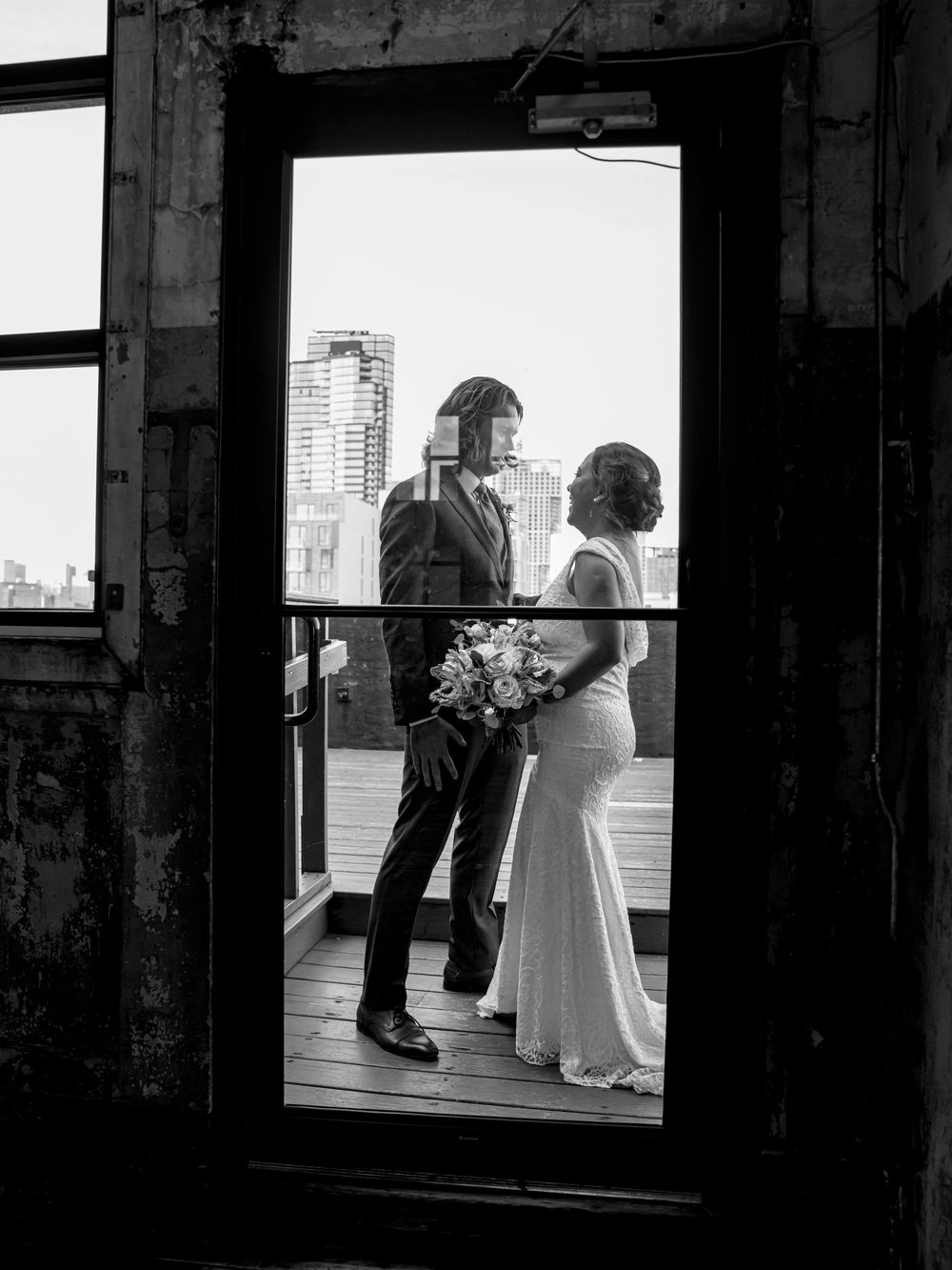 A black and white wedding photo of a couple silhouetted in a doorway against a city skyline.