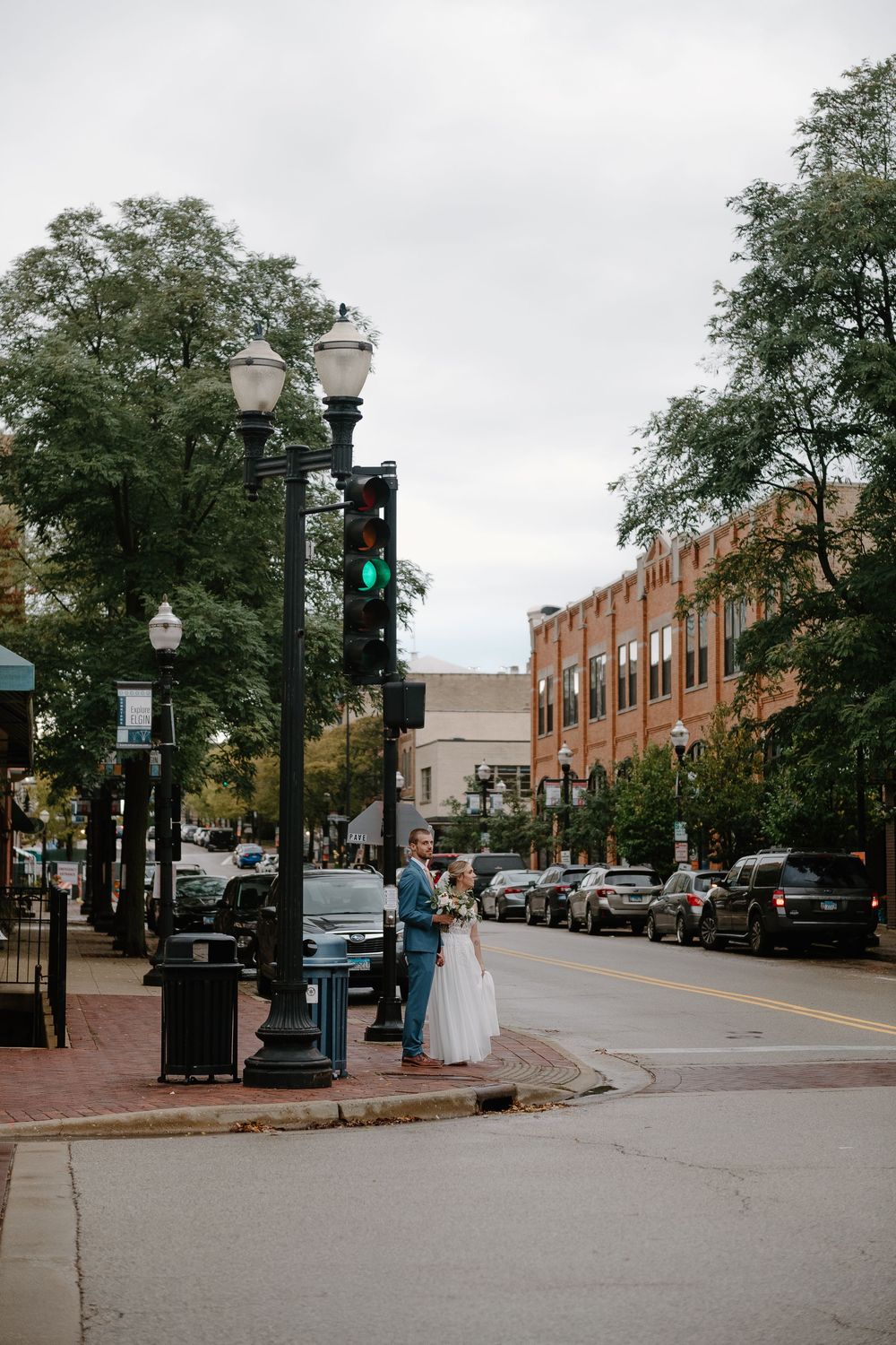 Historic downtown street with brick buildings, vintage lampposts, and parked cars along a tree-lined sidewalk.