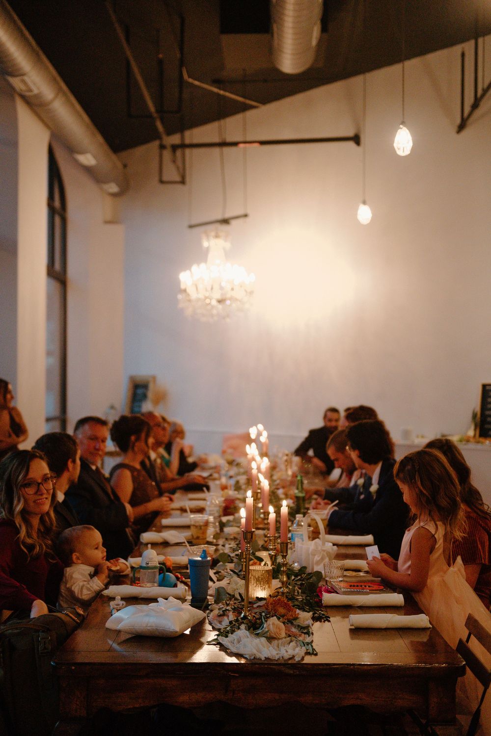 Candlelit wedding reception tables set in an industrial-style venue with white walls and hanging pendant lights.