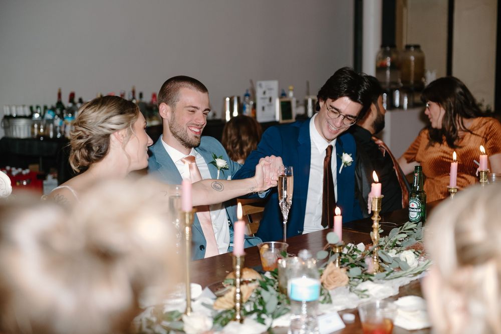 Wedding guests celebrate at an elegant reception with wine glasses and table settings in a dimly lit venue.