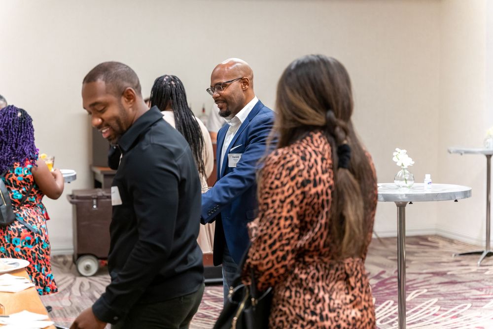 Guests in formal attire mingle and serve themselves at an elegant indoor event with tables.