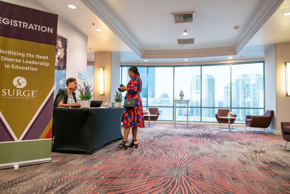 A registration desk at a professional conference with city skyline views through large windows.