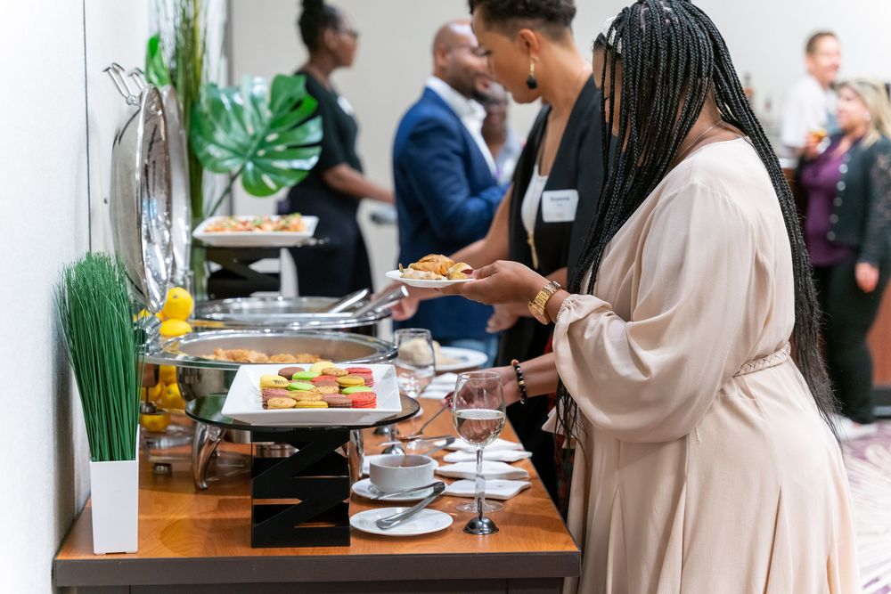 People serve themselves at a catering buffet with decorative plants during an elegant business event.