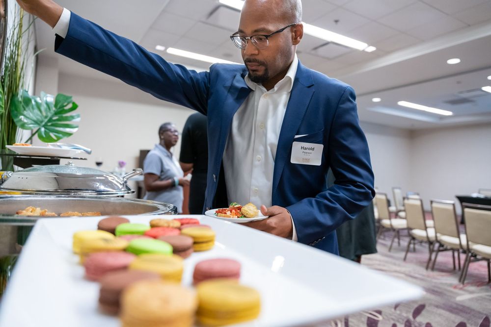 Business professionals are gathered in a conference room around a table with refreshments and pastries.
