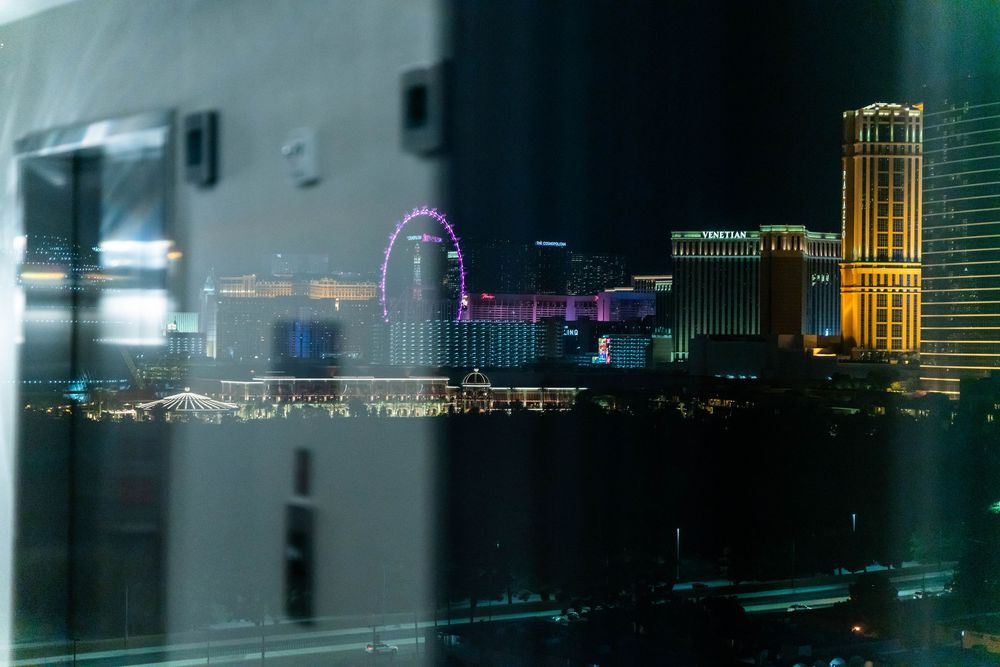 Panoramic night view of a city skyline reflecting on water with illuminated buildings and bright lights.