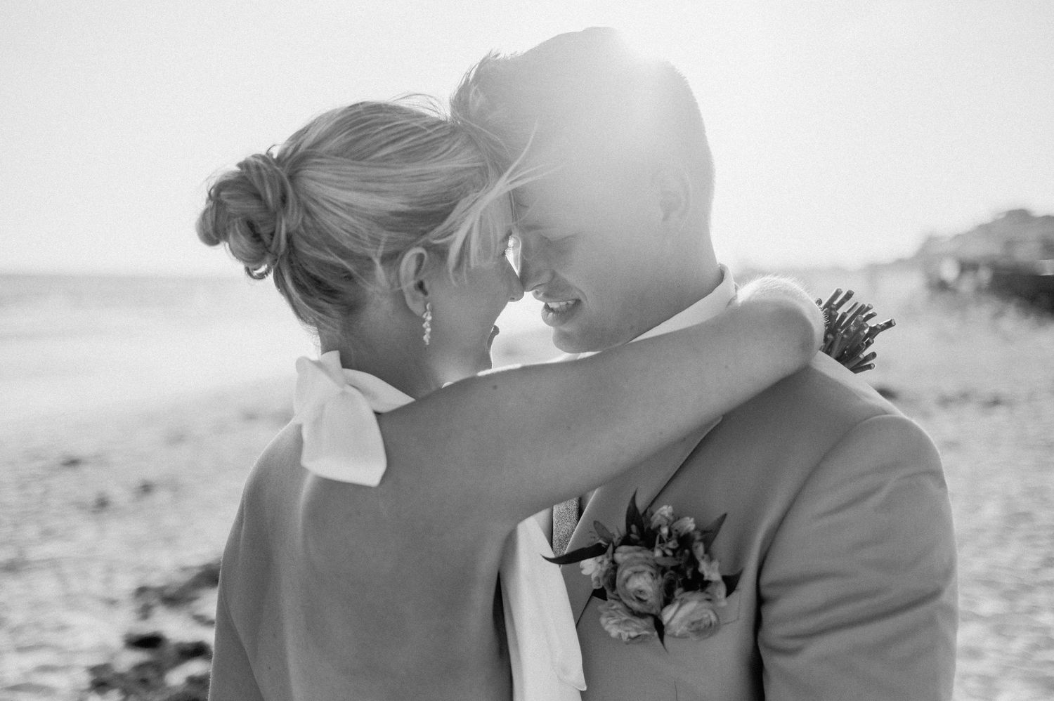 A romantic black and white photograph of an intimate couple embracing outdoors with sunlight behind them.