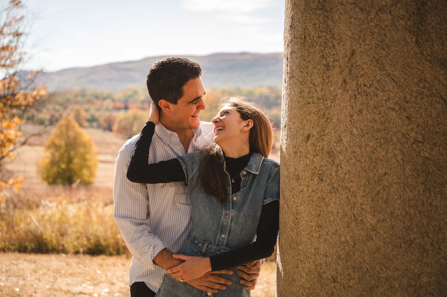A couple gets engaged on a hillside during autumn with a scenic mountain vista in the background.