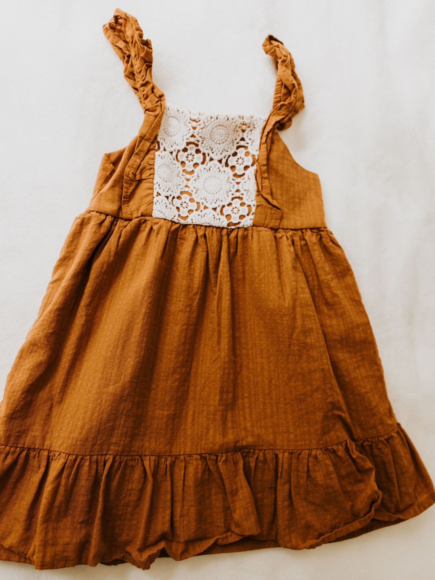 Formal infant outfit with beige vest, white shirt, light blue bow tie, and matching shorts hanging on wooden ladder shelf.