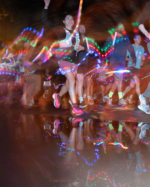 Motion-blur photograph of runners with colourful light trails reflected on wet ground.