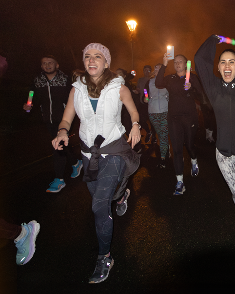 Group of people enjoying a nighttime fitness event with glowing lights and enthusiastic jumping movements.