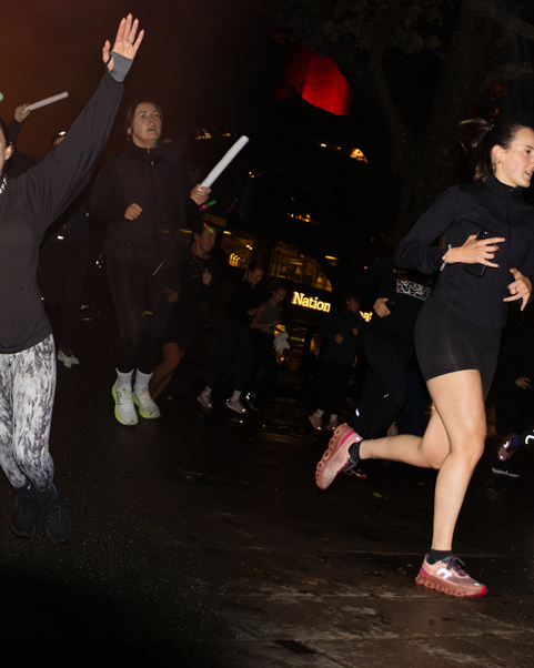 Athletes running and jumping during a night time outdoor fitness event with city lights in background.