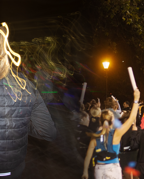 Crowd holding glowing light sticks at night event with street lamp illuminating the scene.