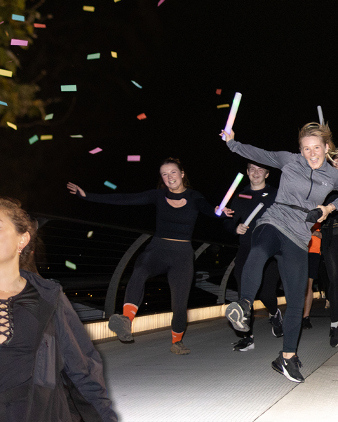 People jumping energetically on a bridge while holding light sticks during a night run.