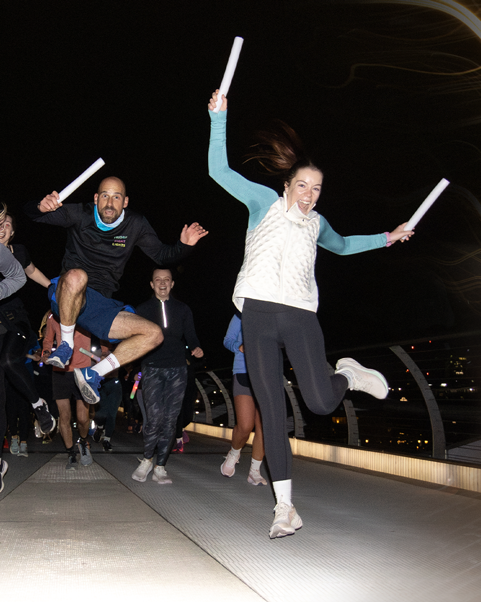 People jumping energetically on a bridge while holding light sticks during a night run.