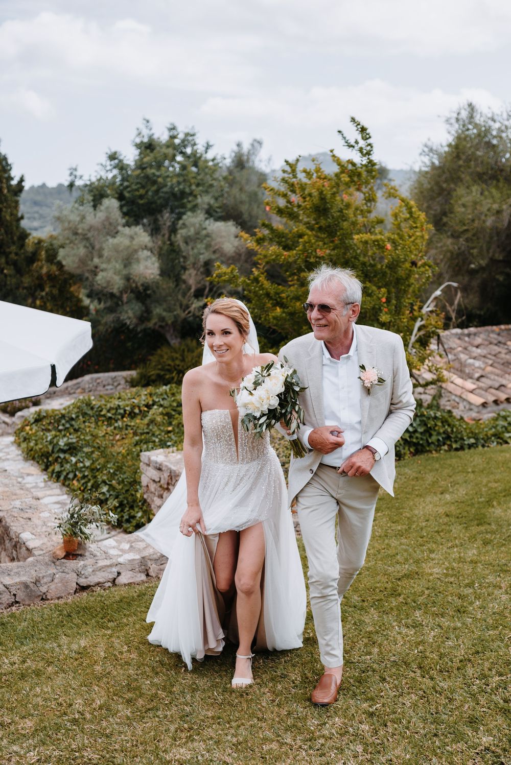 Einzug der Braut mit ihrem Vater auf der Wiese der Finca Xiclati auf Mallorca. Sie im weißen Kleid und er im hellen, leichten Anzug.